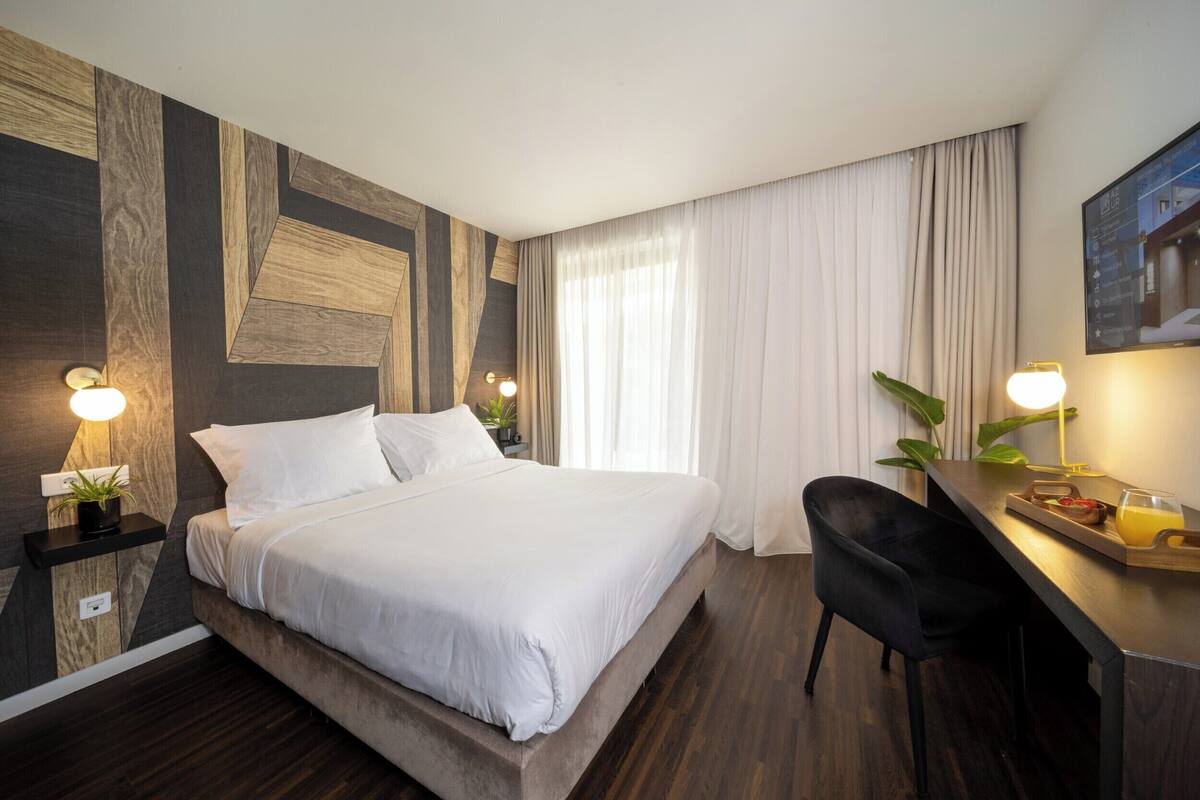 A modern hotel room with a large bed, a desk with a chair, and a TV mounted on the wall.