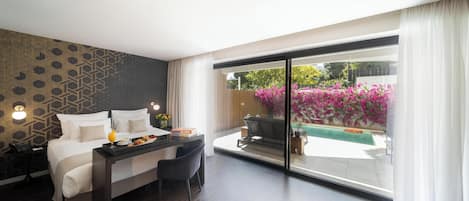 Habitación de hotel con cama, escritorio con una computadora portátil, silla y vista a una piscina y jardín.