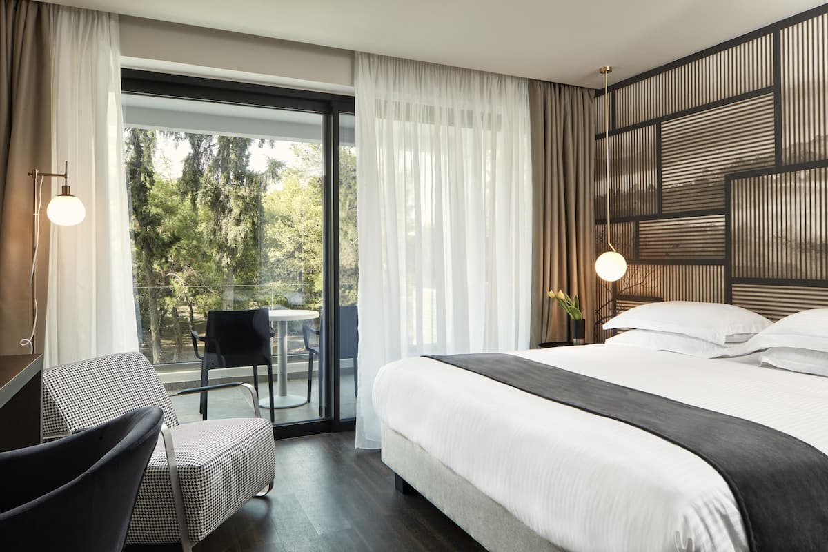A modern hotel room with a large bed, a desk, and a view of the outdoors.