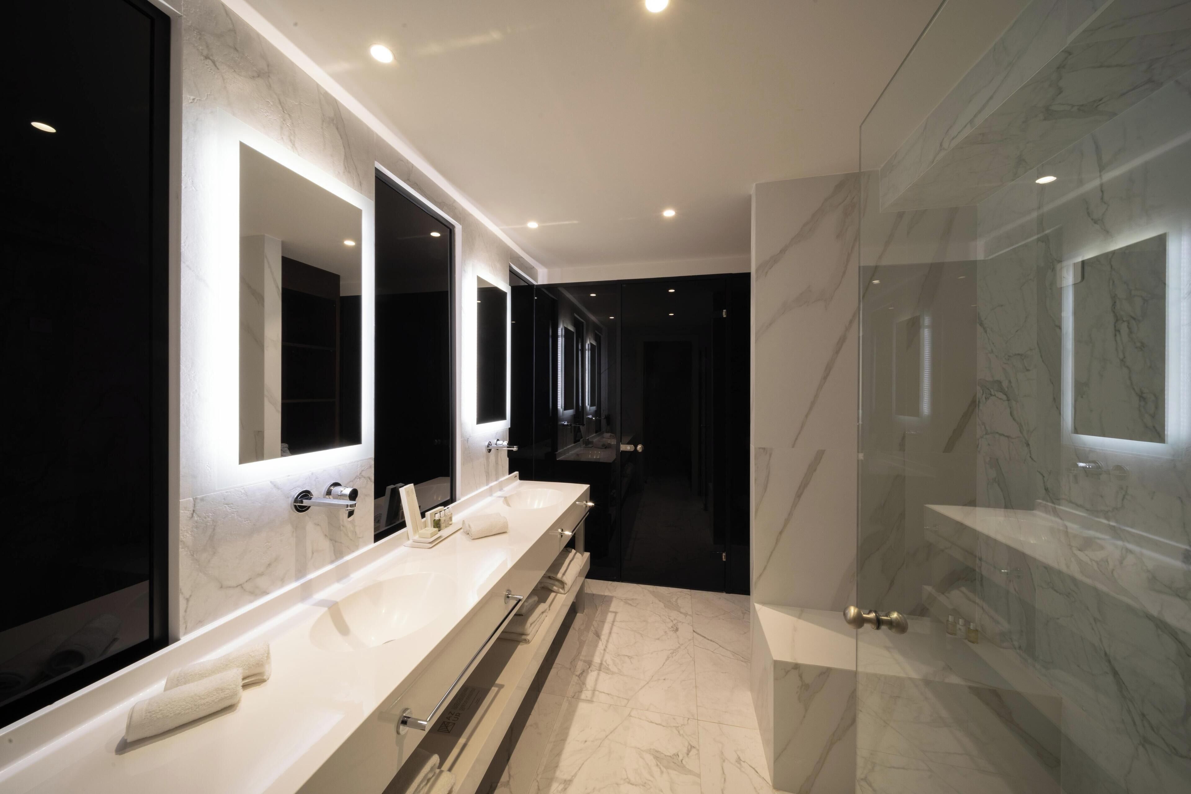 Une salle de bain moderne dotée d’un long meuble-lavabo, de plusieurs miroirs et d’une cabine de douche en verre.