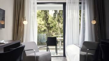 A hotel room with a bed, two chairs, a desk, and a view of a balcony with a table and chair.