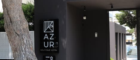 A modern building with a sign for "AZUR Boutique Hotel" and a tree in front.