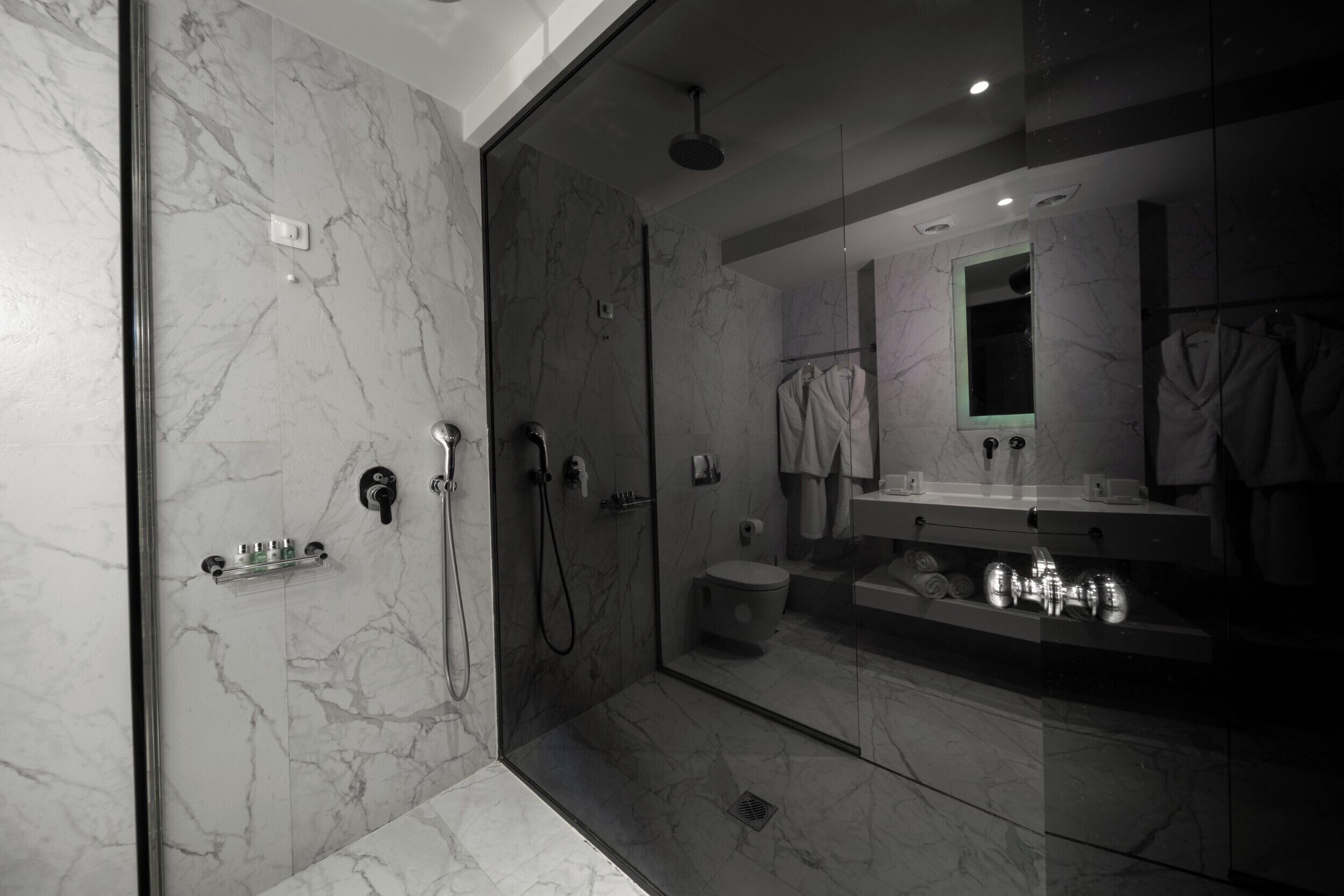 A modern bathroom with a glass-enclosed shower, marble walls, and a large mirror.