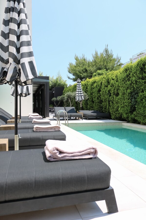 A poolside area with lounge chairs and towels, a pool, and a hedge in the background.