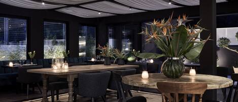 A modern dining area with a round wooden table, black chairs, and a large potted plant.