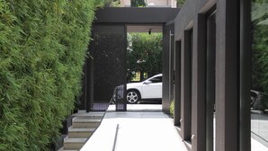 A modern building with a glass facade, a staircase leading to a car parked outside, and a neatly trimmed hedge. - Azur Hotel (Vari-Voula-Vouliagmeni)