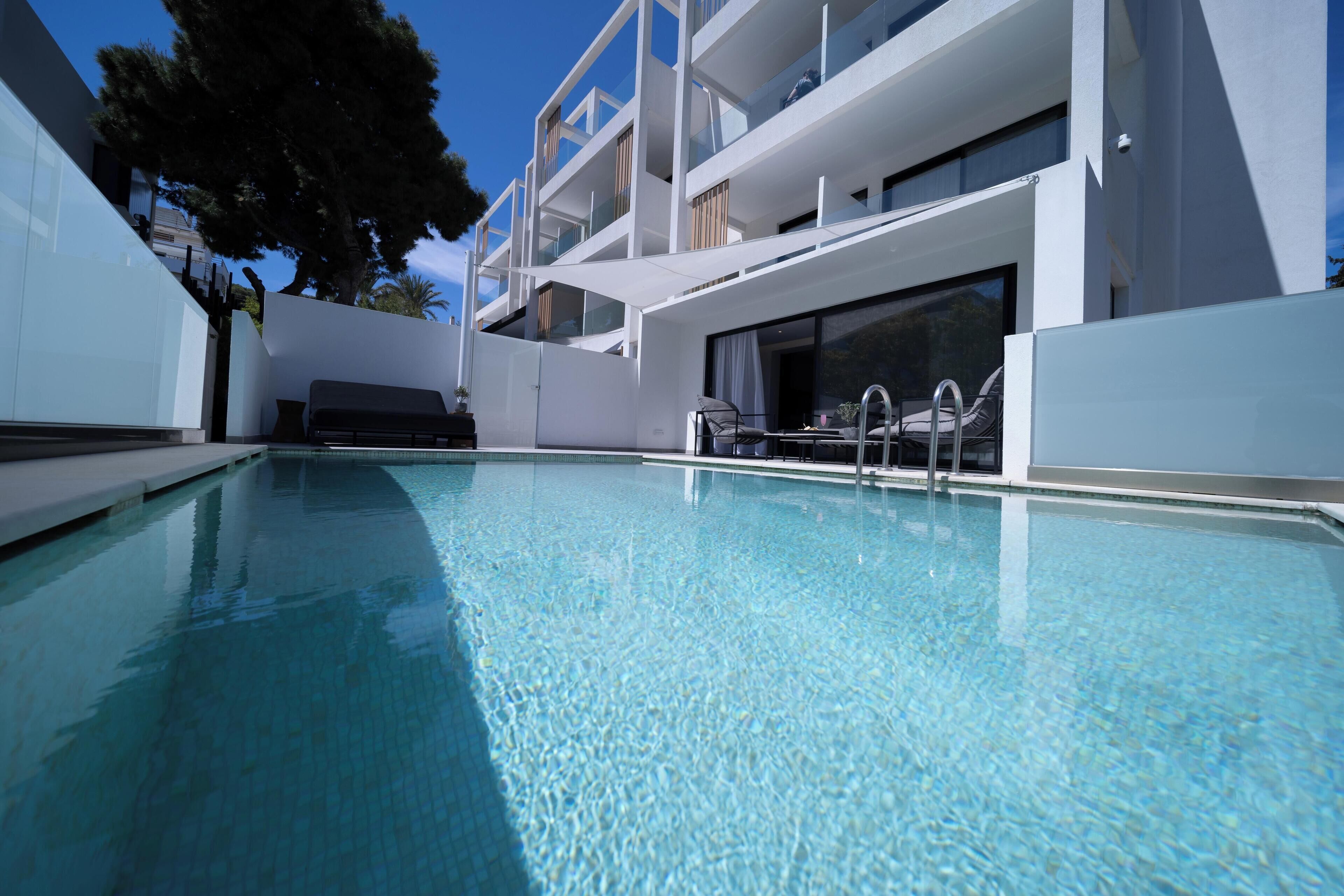 A modern building with a swimming pool, outdoor seating, and a clear blue sky.