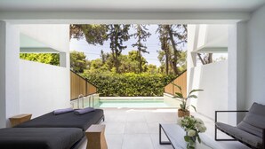 A modern spa room with two beds, a small table, a bench, and a view of a pool and greenery. - Azur Hotel (Vari-Voula-Vouliagmeni)