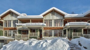 A multi-story chalet with a snow-covered roof and a wooden deck. - Ski in Ski out condo with private Hot Tub backing on Golf course. 2 bed 2 bath. (Sun Peaks)