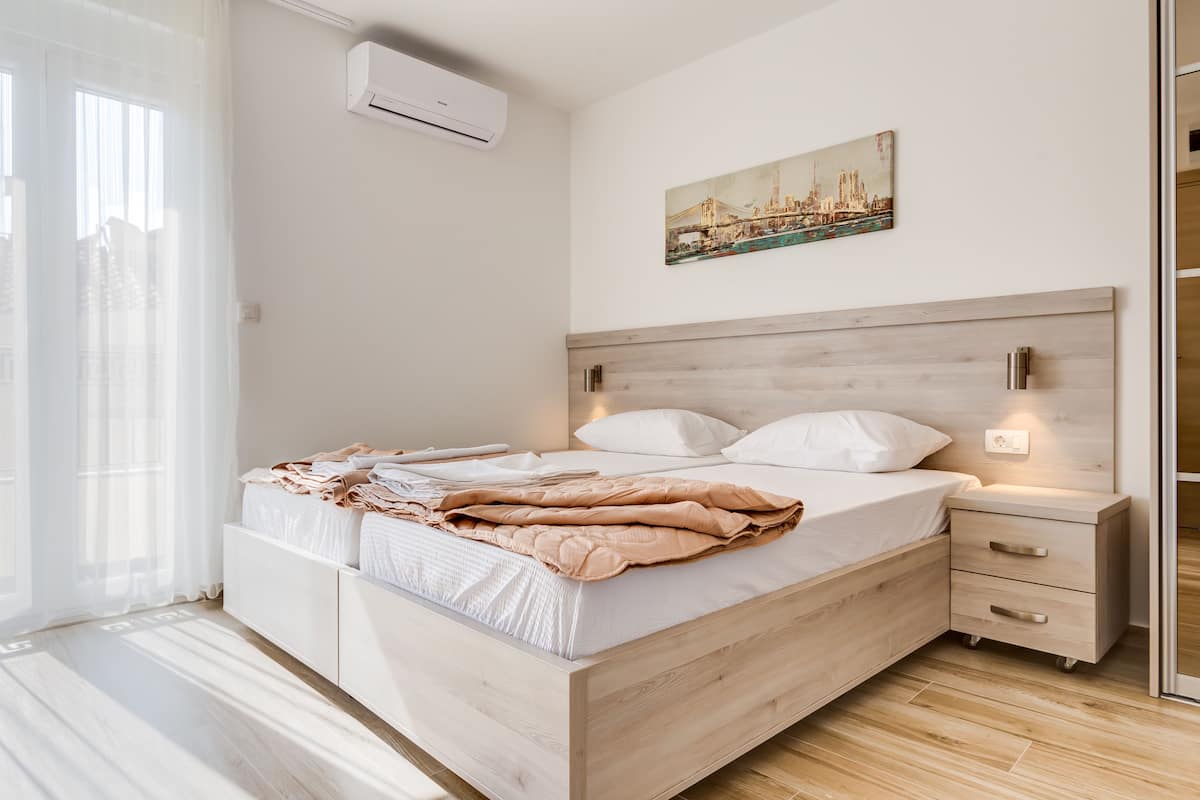 A modern bedroom with a wooden bed, white bedding, a cityscape painting, and a nightstand with a lamp.