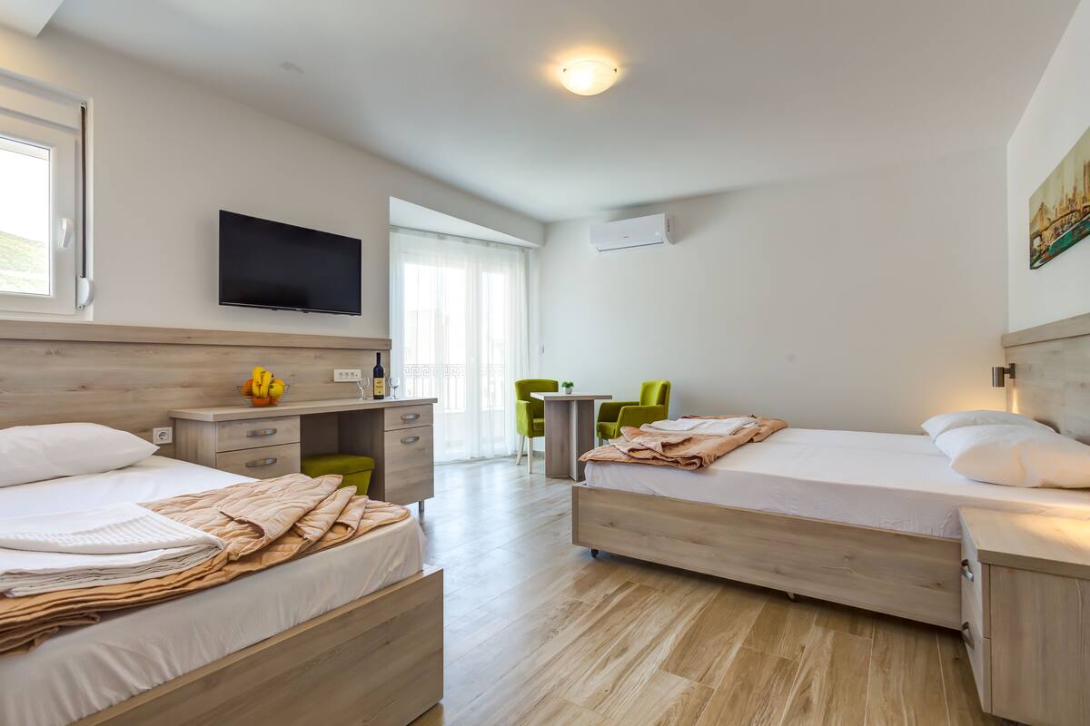 A modern hotel room with two beds, a desk, a TV, and a small table.