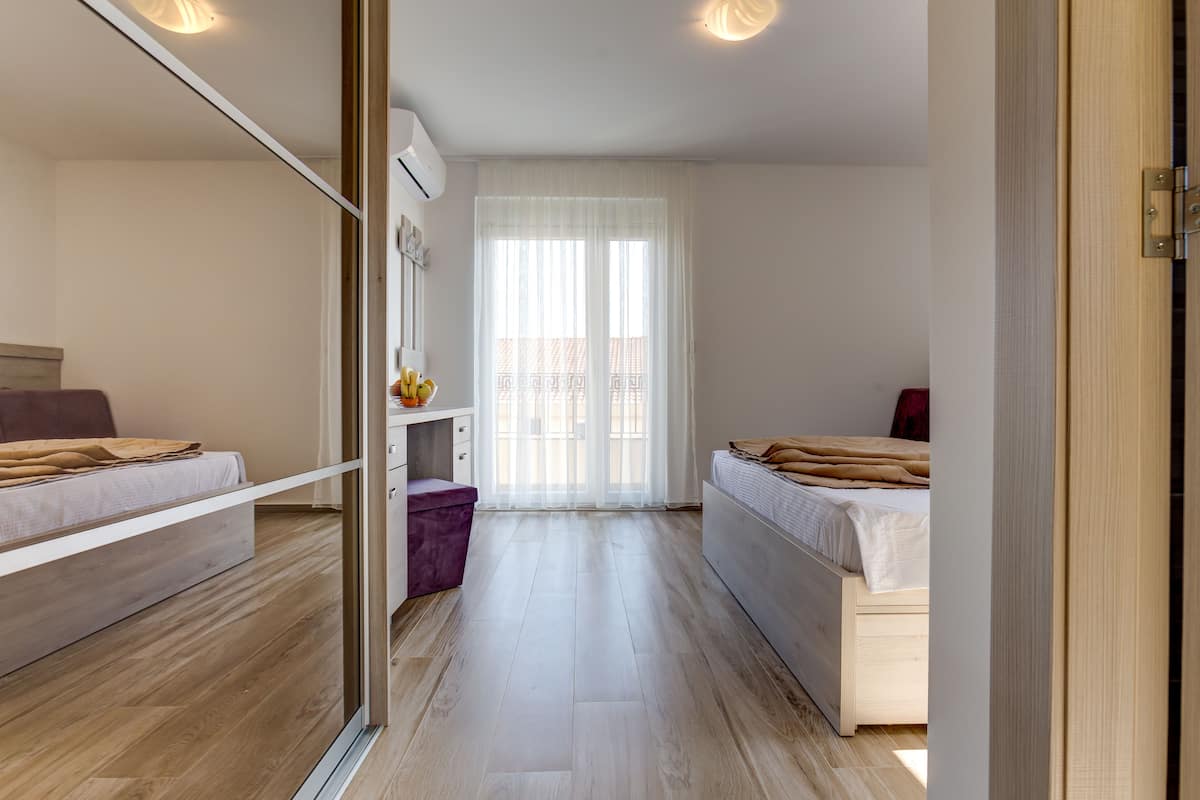 A modern bedroom with two beds, a wardrobe, and a window with sheer curtains.