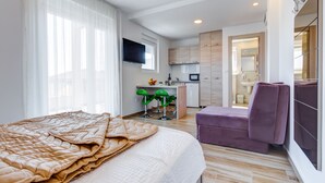 Ein modernes Hotelzimmer mit einem großen Bett, einem kleinen Schreibtisch, einem Fernseher und einem durchgegangene Tür erkennbaren Badezimmer.