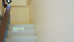 Eine Treppe mit weißen Stufen und einem hölzernen Geländer, die zu einer Zwischenebene mit einer Lampe führt.