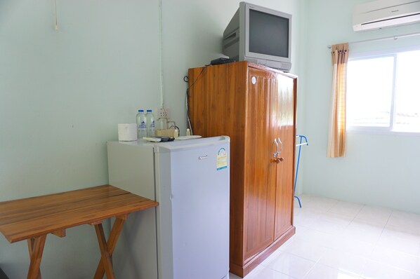 A compact room with a wooden cabinet, a small refrigerator, a wooden table, and a television on top of the cabinet.