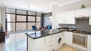 A modern kitchen with a large island, a washing machine, and a built-in oven. - Hill House 1 Bedroom (Cape Town)