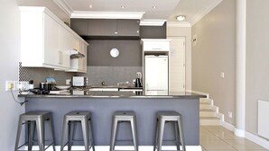 A modern kitchen with a central island, bar stools, and a staircase leading to another level. - Hill House 1 Bedroom (Cape Town)