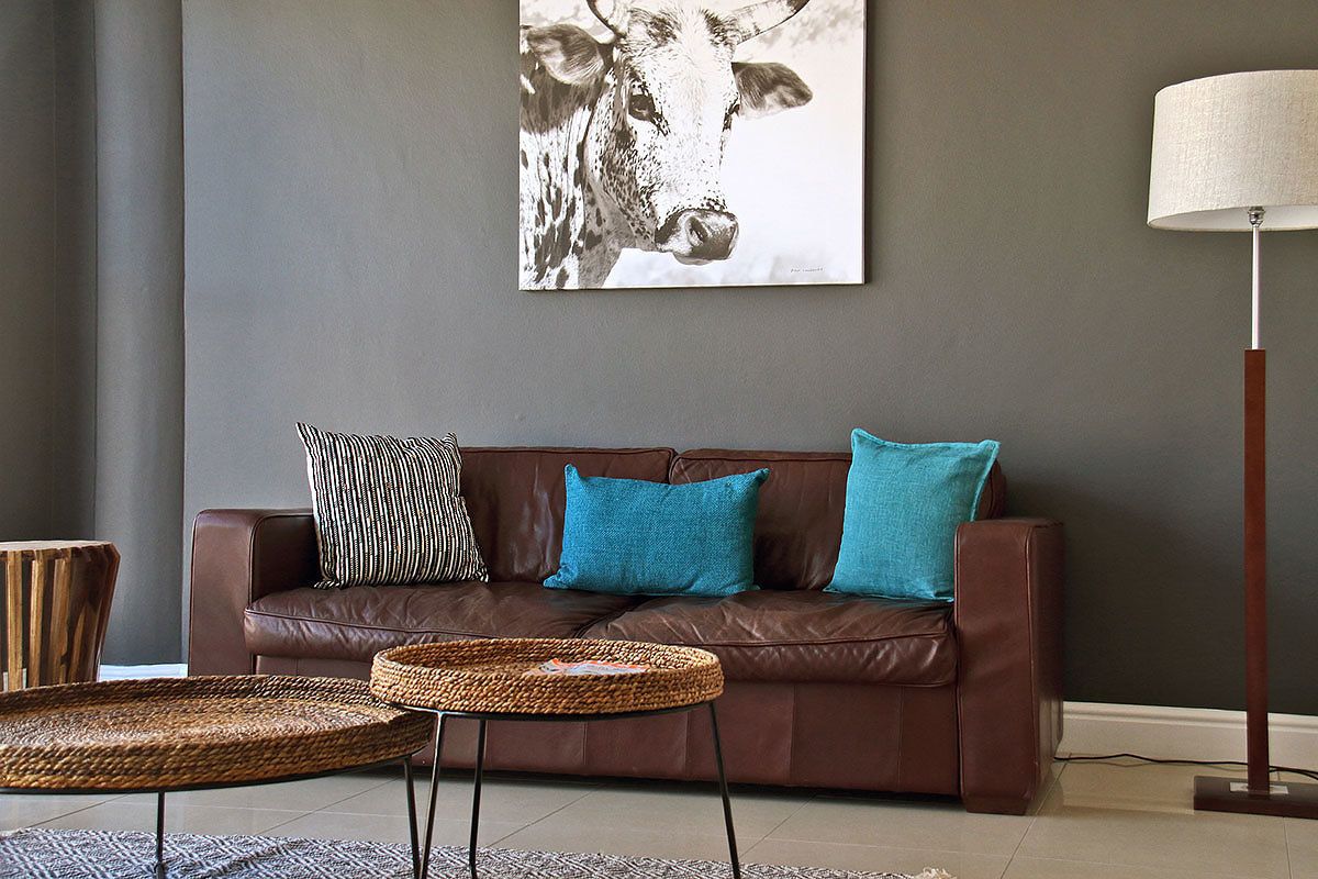 A brown leather sofa with two blue cushions, a woven side table, and a wall-mounted lamp.