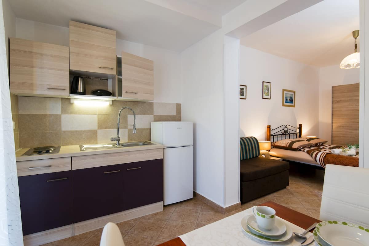 A compact kitchen with modern appliances, a dining area with a table set for two, and a cozy bedroom with a bed and bedside table.