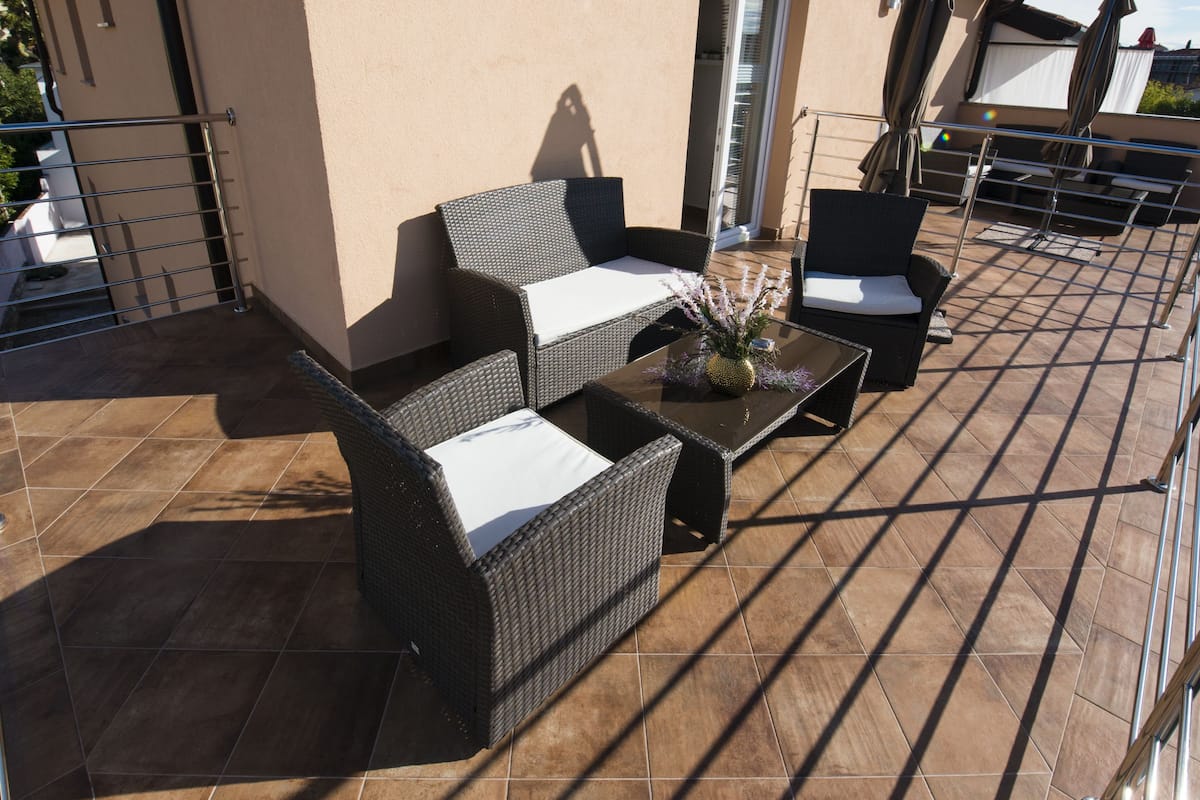 A patio with wicker furniture, a glass table, and a vase with flowers.