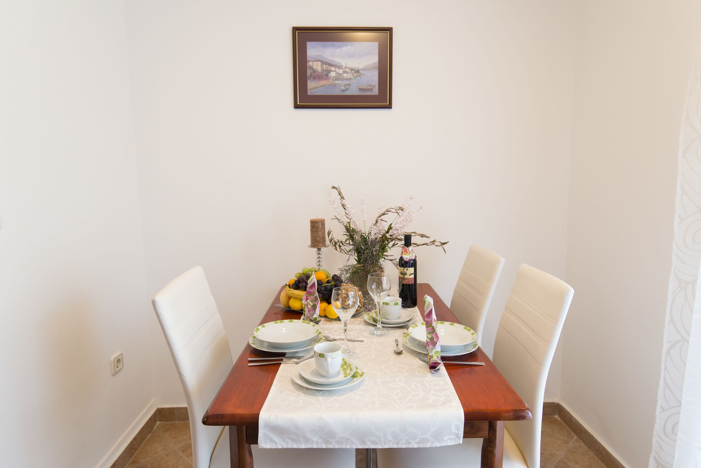 Une table à manger dressée avec de l’assiette blanche, des bols et des couverts, entourée de chaises blanches.