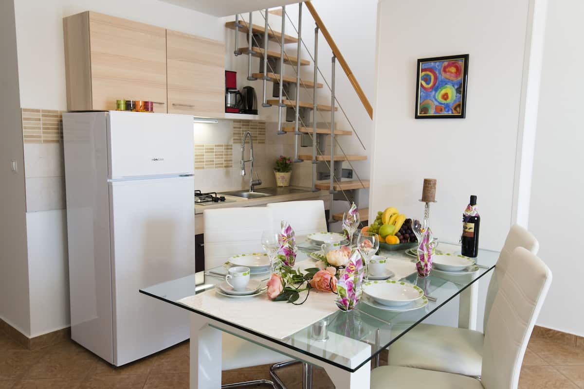 A modern kitchen with a white refrigerator, wooden cabinets, and a glass dining table set with plates, glasses, and flowers.