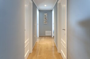 A hallway with wooden flooring, white doors, and a vent on the wall.