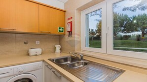 Una cocina con armarios de madera, lavadora integrada, tostadora y un lavabo con ventana arriba.