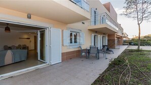 Un apartamento moderno con entrada por puerta corredera de vidrio, un balcón con mobiliario de exterior y un pequeño jardín.