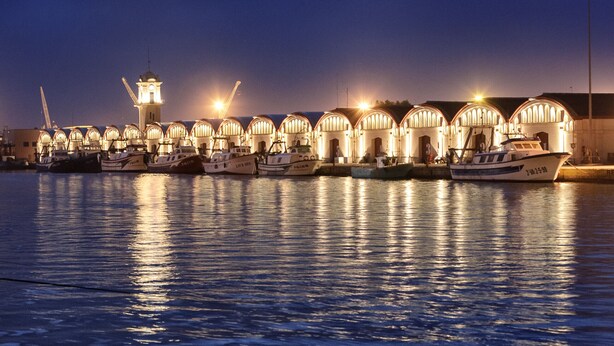 Un puerto deportivo de noche con barcos amarrados y un edificio con ventanas arqueadas.