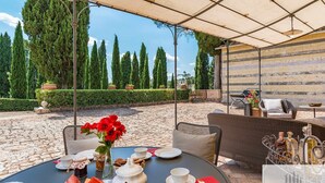 Een terras buiten met ronde tafels klaar voor dineren, omringd door groen en een stenen muur.