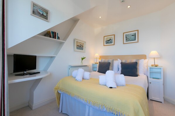 A neatly arranged bedroom with a bed, bedside tables, a television, and framed pictures on the walls. - SeaCrest, St Ives – Sleeps 10 – On-Site Parking – Sea Views (St Ives)