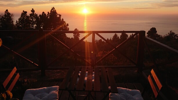 Una terraza de madera con dos sillones de descanso mirando al atardecer sobre el océano.