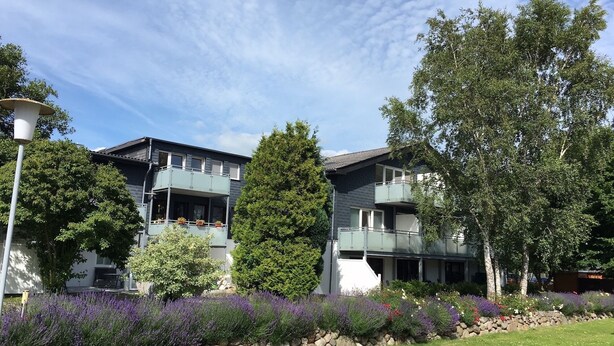 A two-story building with balconies, surrounded by greenery and a stone wall.