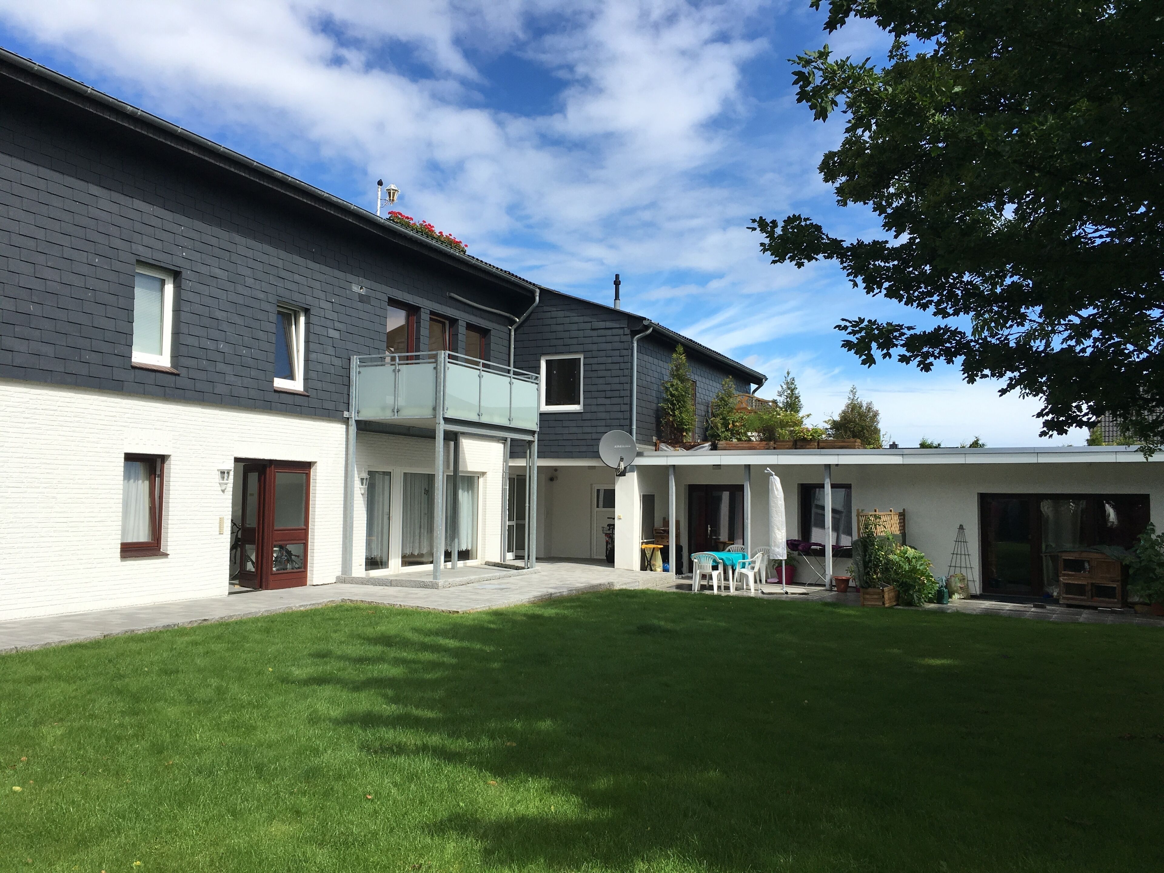 A modern two-story house with a balcony, a covered patio, and a well-maintained lawn.