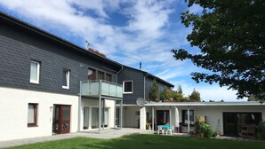 A modern two-story house with a balcony, a covered patio, and a well-maintained lawn.