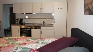 A compact bedroom with a bed, a sofa, and a kitchenette with basic appliances.