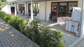 A building with a covered patio area featuring outdoor seating and a white wicker chair.