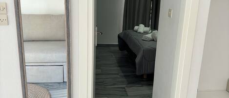 A hallway leading to a bedroom with a bed, a mirror, and a small window.
