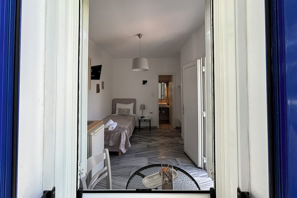 A narrow hallway leading to a bedroom with a bed, bedside table, and a small table with a vase.
