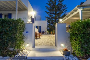 A courtyard with a stone floor, outdoor furniture, and a large tree. - Marioly Studios (Paros)