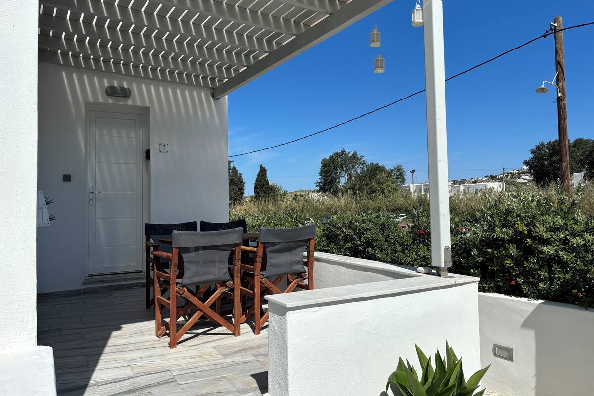 A white building with a covered patio, outdoor seating, and a view of the surrounding landscape.