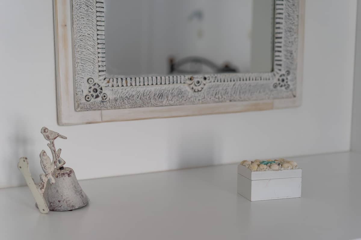 A white wall with a decorative mirror and a small white box with seashells.