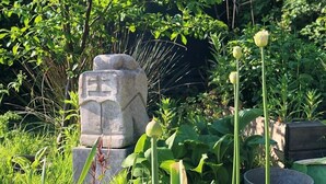 Un monumento de piedra rodeado de abundante vegetación y plantas con flores.