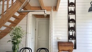 Un área de comedor con una escalera de madera, un jarrón con flores y un estante en la pared con adornos.