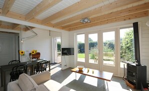 A spacious living area with a wooden ceiling, a sofa, a dining table, and a TV.