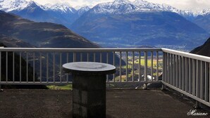 Un balcón con mesa de piedra, que ofrece vistas a montañas nevadas y un valle.