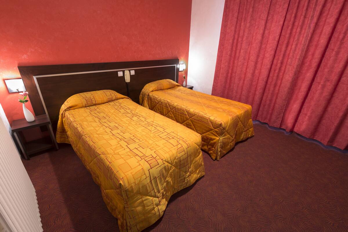 Una habitación de hotel con dos camas individuales, una mesita de noche con lámpara y una cortina roja.