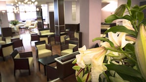 Un hall de hotel con zonas de estar, una recepción y una planta grande con flores.