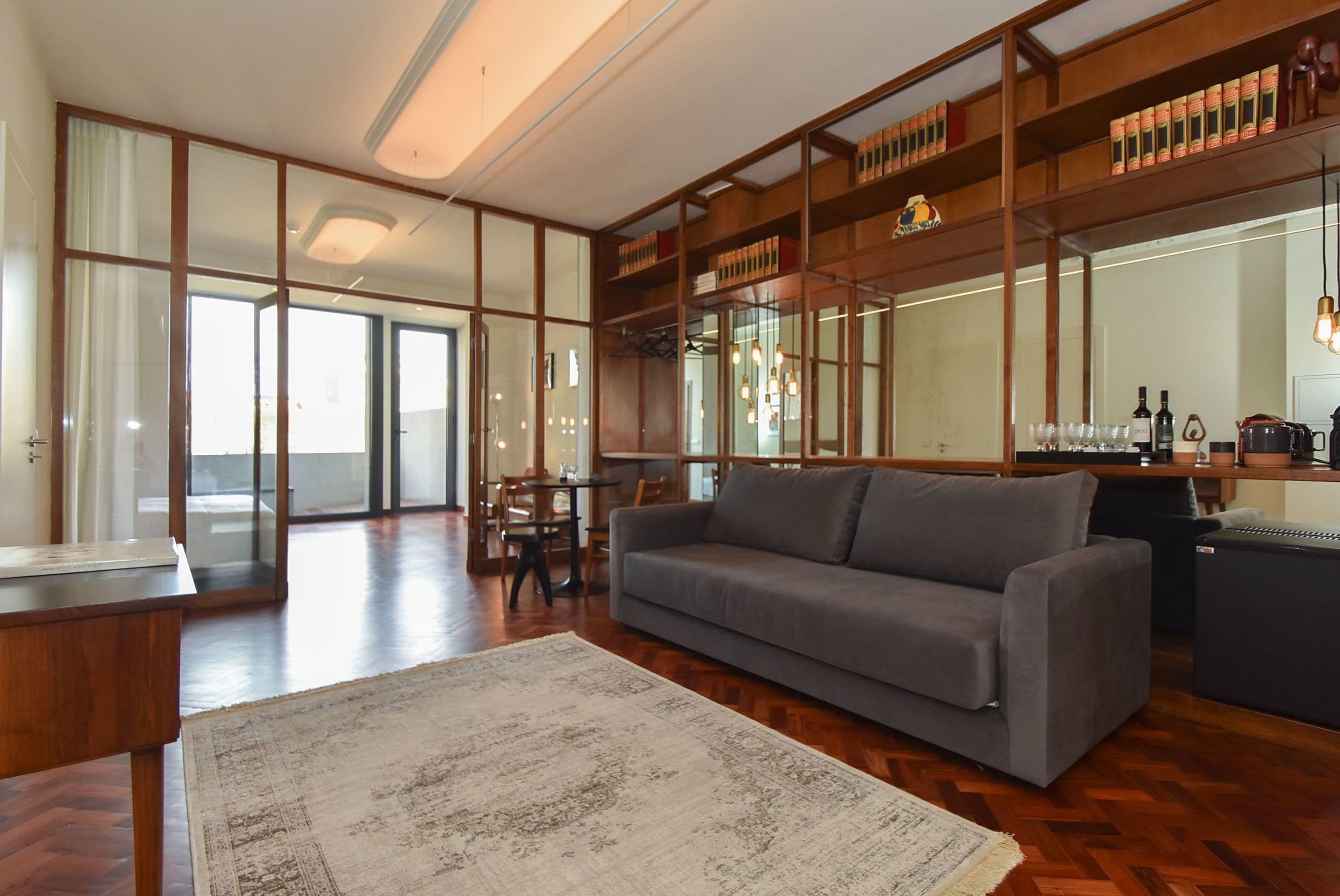 Un salon spacieux avec un canapé gris, un parquet en bois et une grande fenêtre.